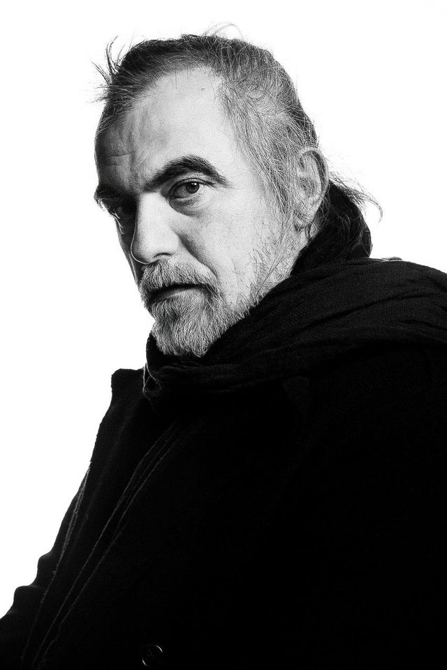 Bearded man in a black coat and scarf, stark high-contrast black-and-white portrait