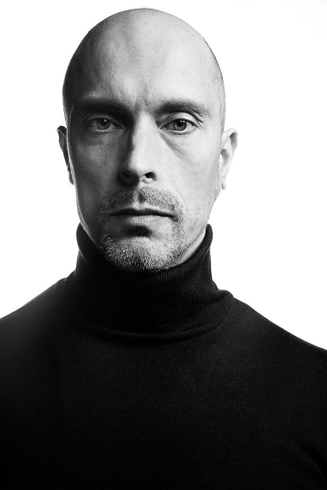 Bald man in a black turtleneck, stark high-contrast black-and-white portrait lighting