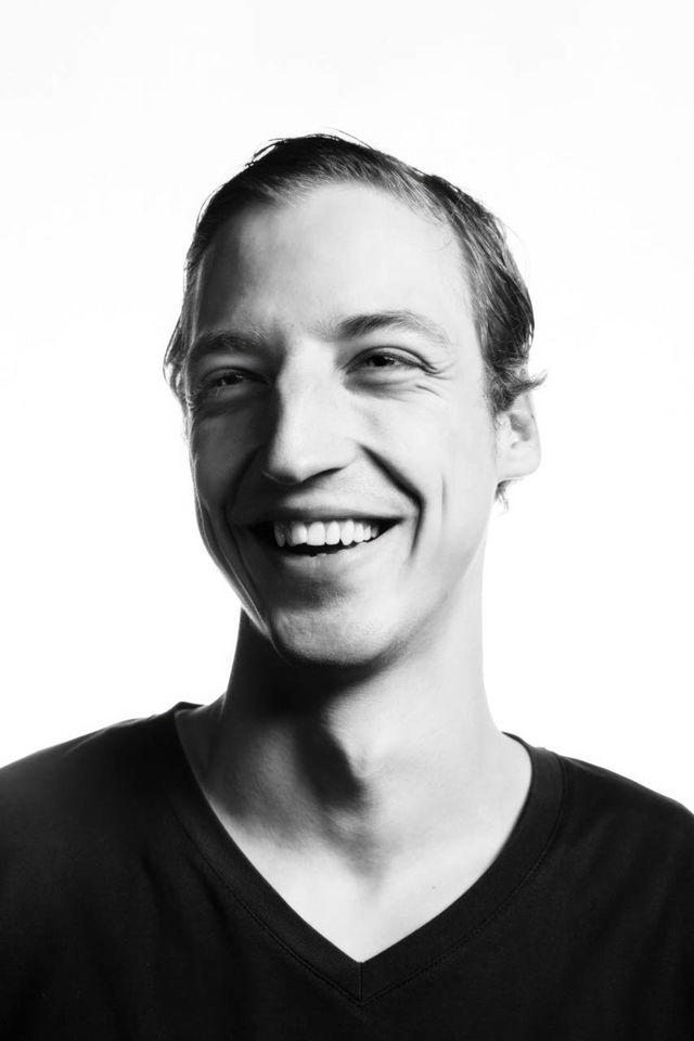 Smiling man in a high-contrast black-and-white studio portrait with stark lighting