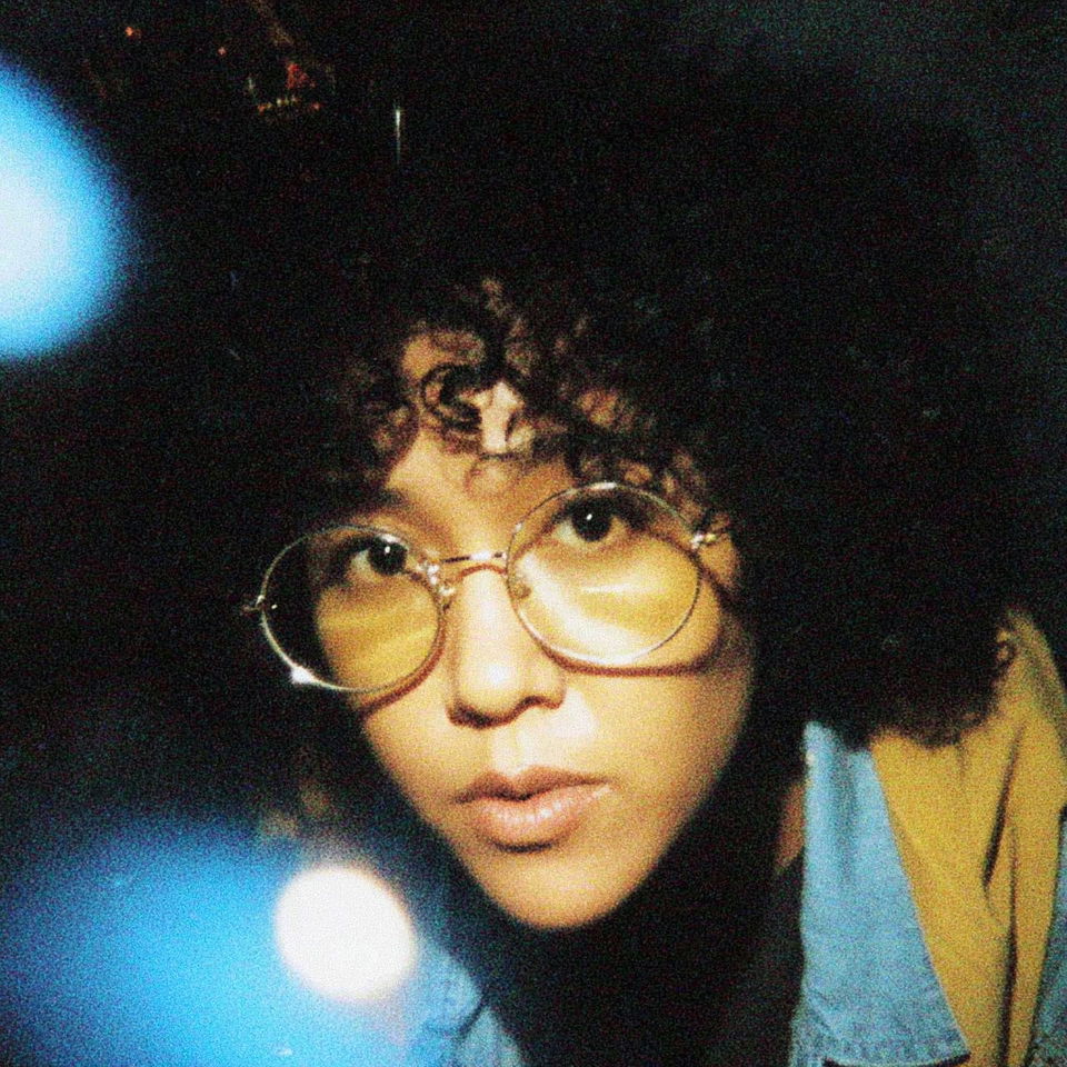 Curly-haired librarian with round glasses, grainy flash photography in warm tones
