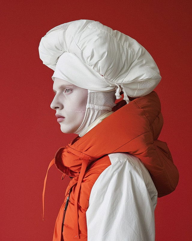 Profiled model in sculptural white headwear and orange puffer clothing, against a red backdrop, Midjourney V6